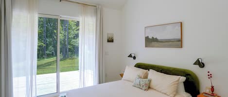 Une chambre à coucher avec un lit, une fenêtre avec des rideaux, un tableau au mur et une table de chevet avec une lampe.