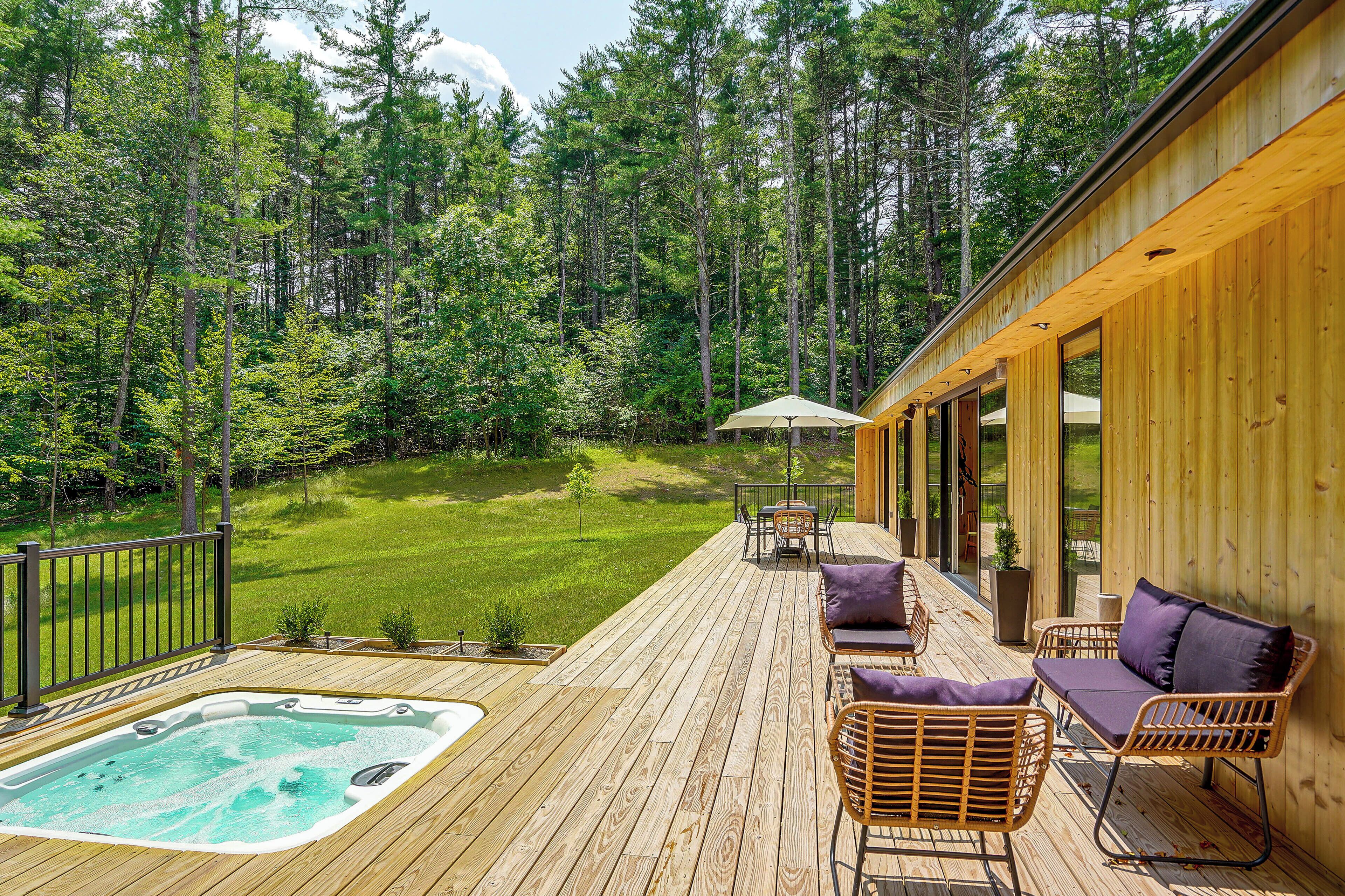 A wooden deck with a hot tub, outdoor furniture, and a view of a forest.
