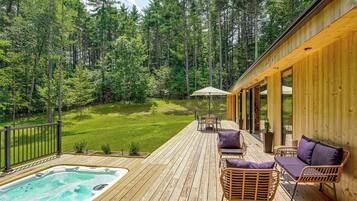 Um deck de madeira com hidromassagem, móveis de exterior e vista para uma floresta.