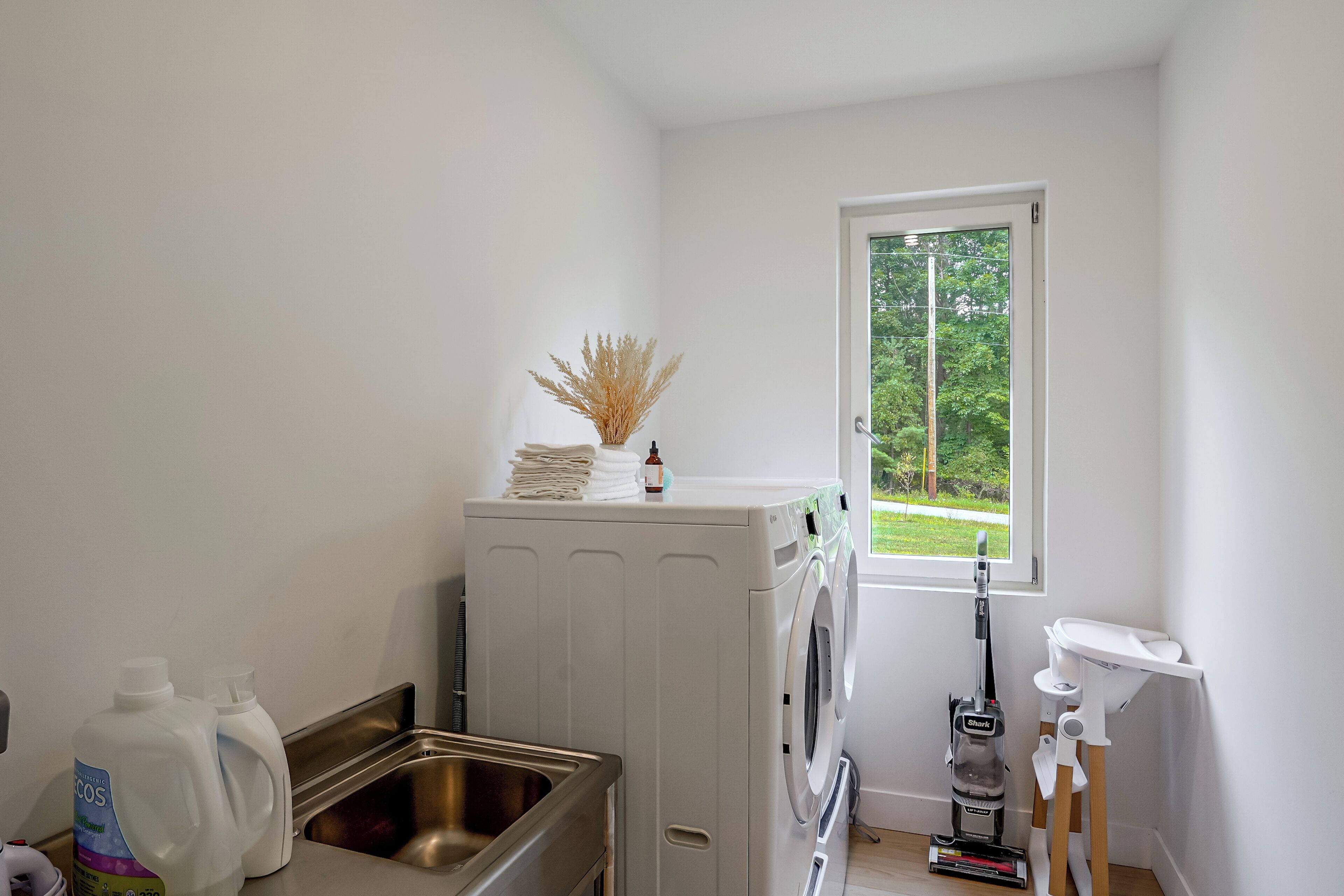 A laundry room with a washing machine, a sink, and a window with a view of greenery.
