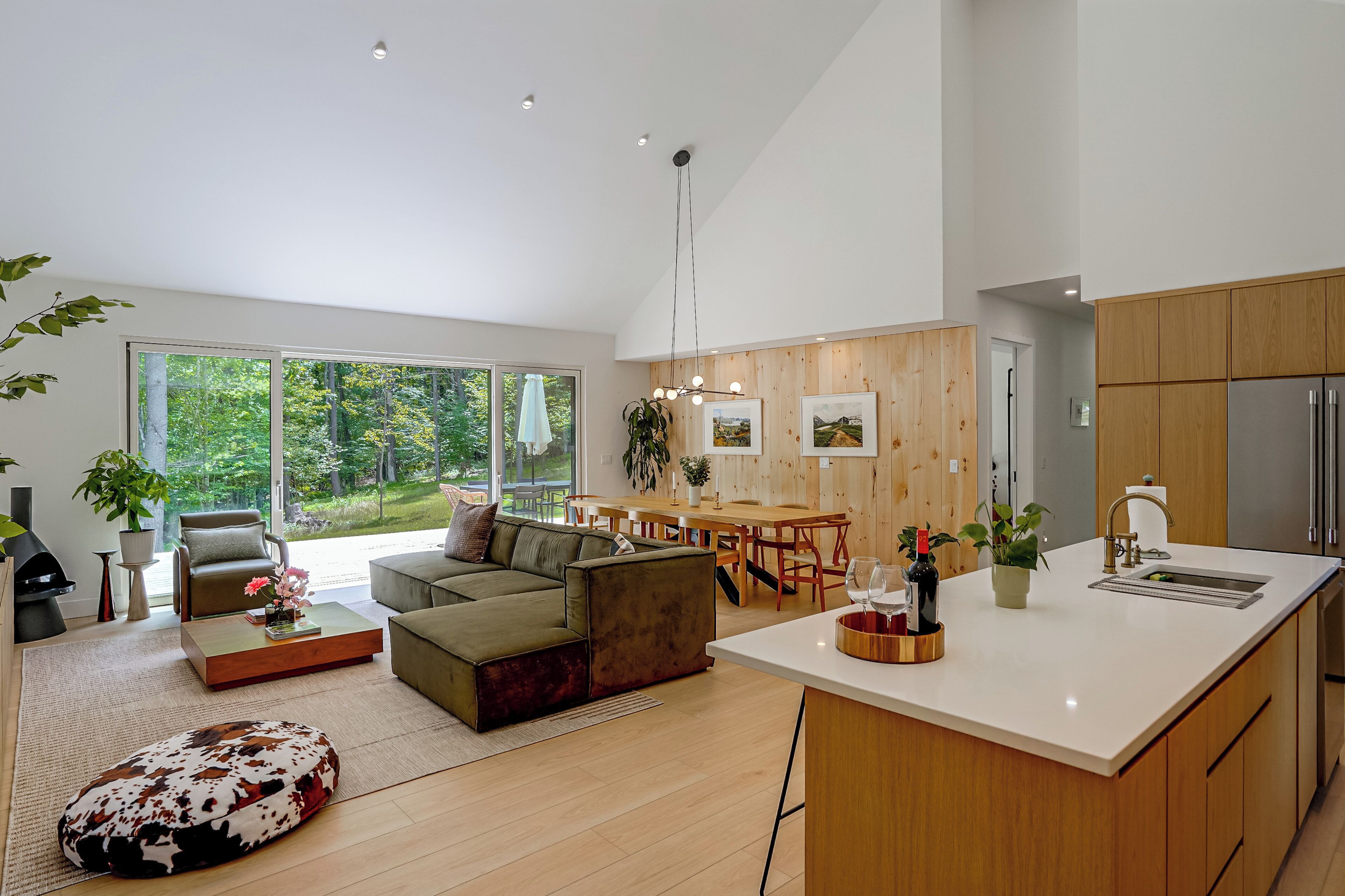 A modern open-plan living and dining area with a large window, wooden flooring, and a central island with a sink.