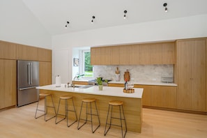 A modern kitchen with wooden cabinets, a stainless steel refrigerator, a large island with stools, and pendant lighting. - Catskills New Build w/ Private Hot Tub & Fire Pit! (Cairo)