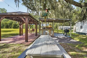 Ein Außenbereich mit einer Holz-Pergola, einem Picknicktisch und einem Grill.