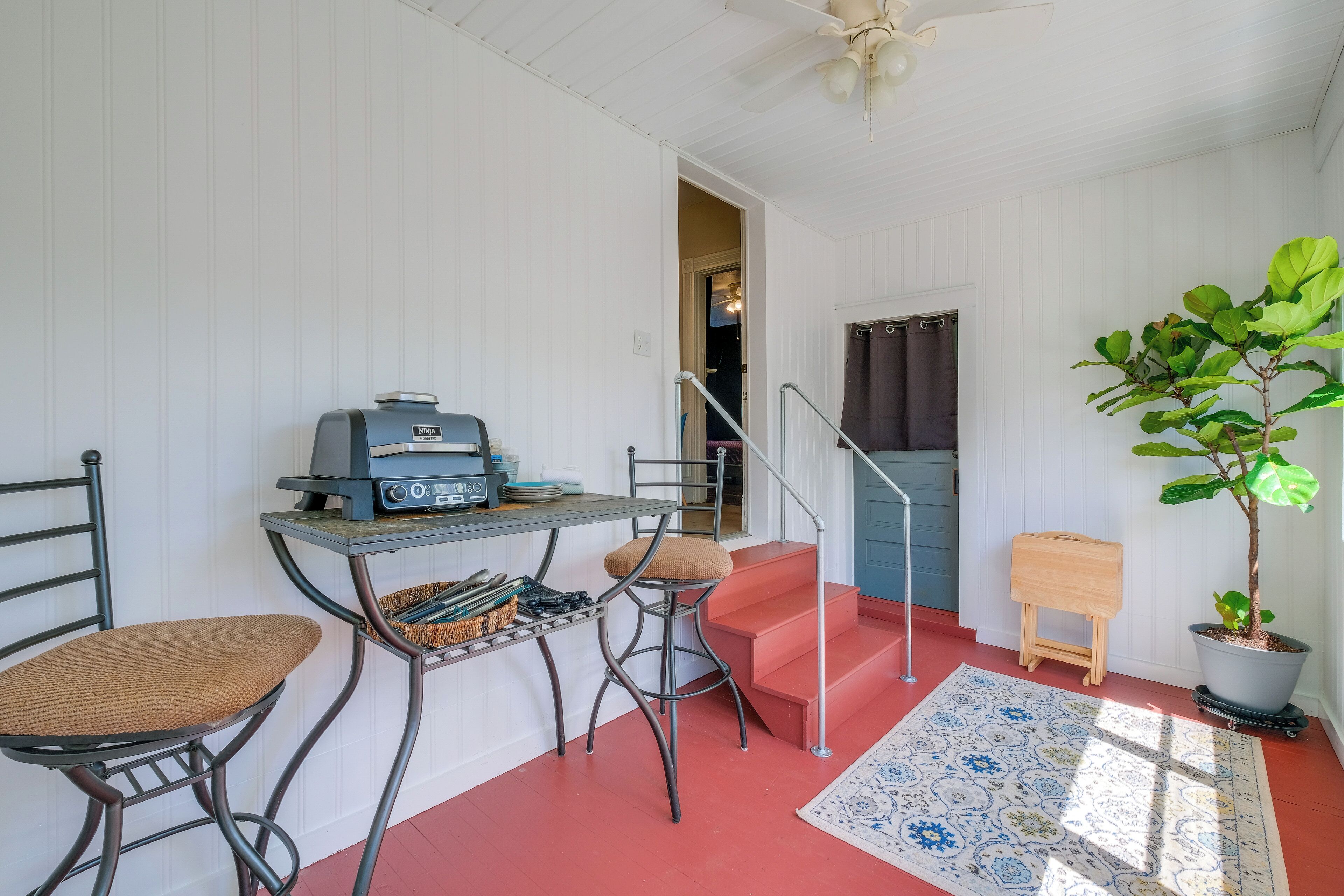 A compact room with a kitchenette, a dining area with two chairs, a small table, a potted plant, and a staircase.