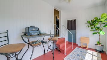 A compact room with a kitchenette, a dining area with two chairs, a small table, a potted plant, and a staircase.