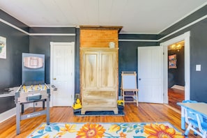 A room with a wooden cabinet, a foosball table, a colorful rug, and a blue table with chairs.