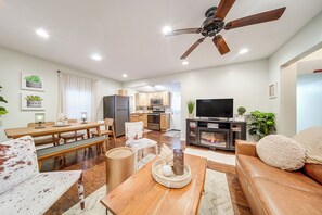 A modern living room with a wooden dining table, a sofa, a TV, and a ceiling fan. - Dual Cottage Escape Walkable to Gotl Strip (Geneva)