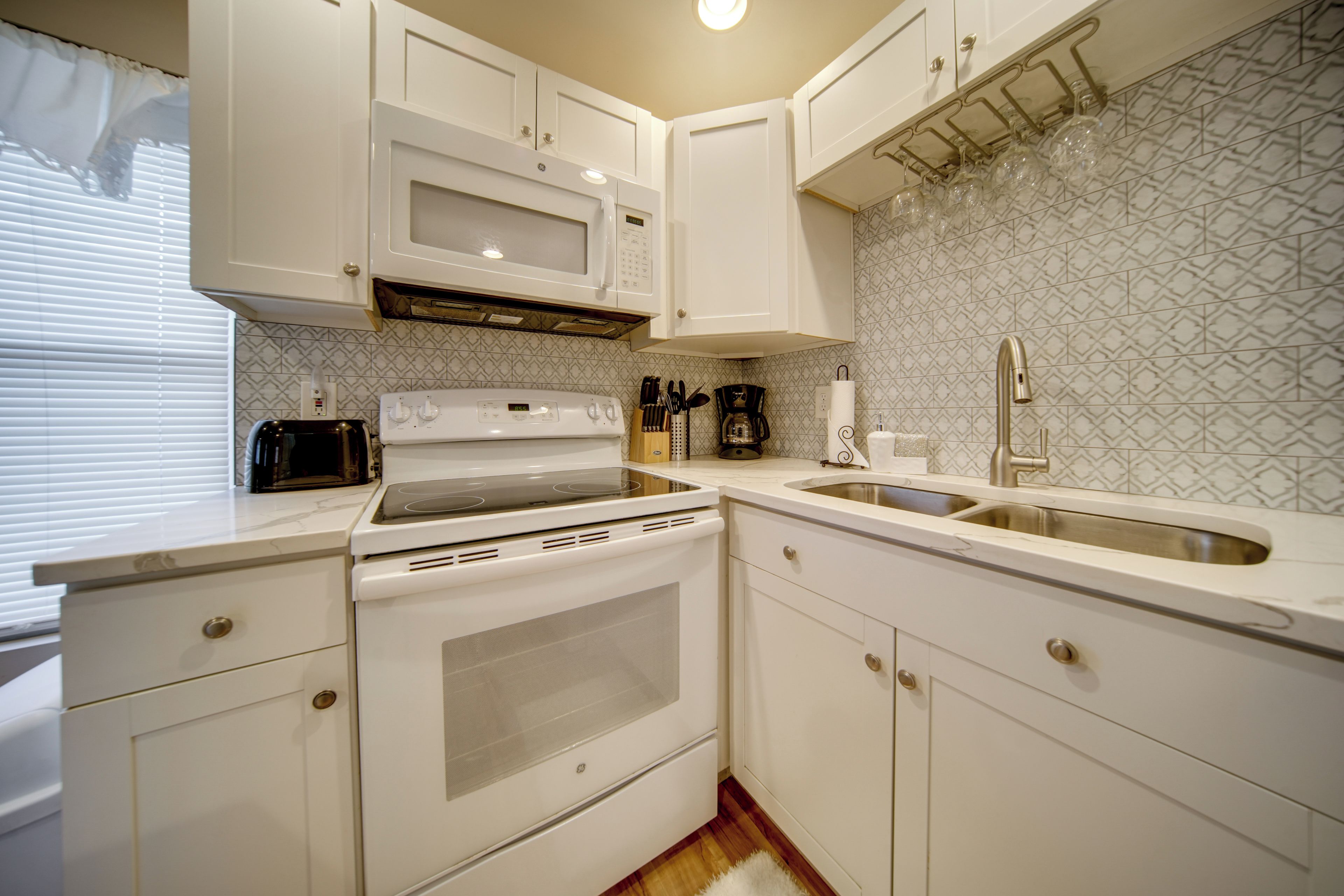 A modern kitchen with white cabinets, a built-in microwave, a stove, and a sink.