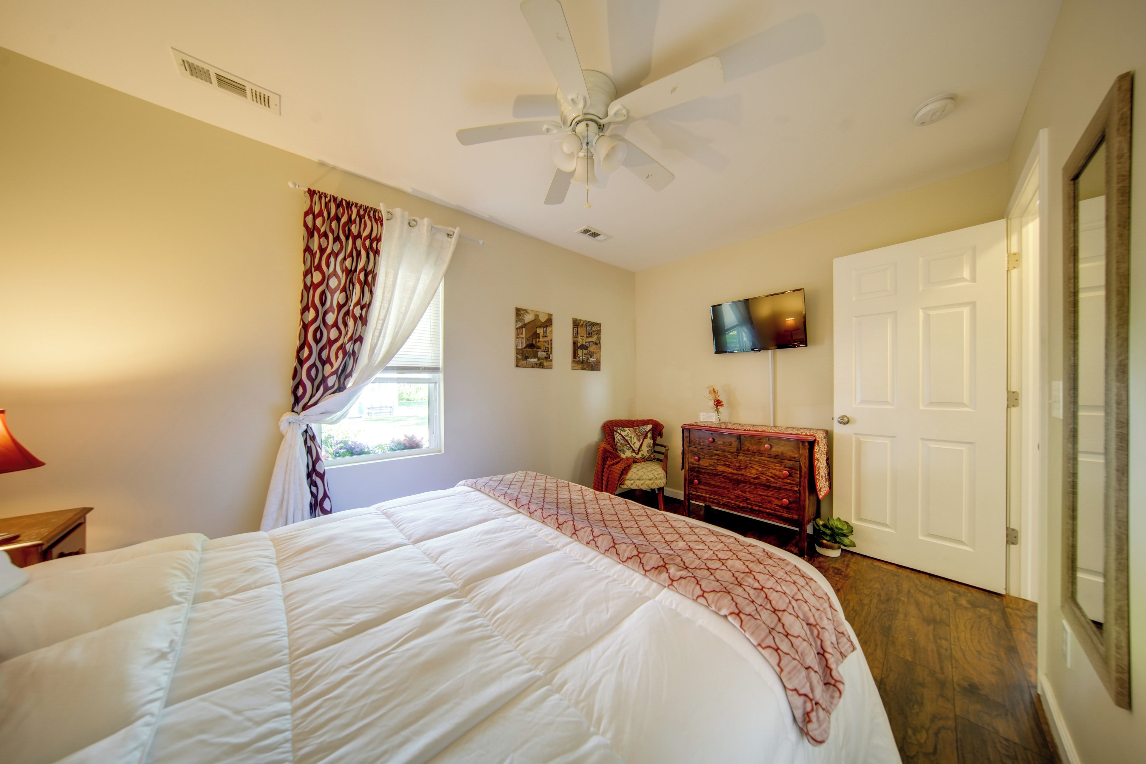 A bedroom with a bed, a ceiling fan, a dresser, a television, and a door.