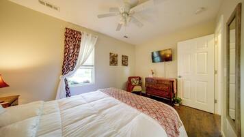 A bedroom with a bed, a ceiling fan, a dresser, a television, and a door.