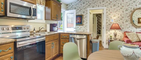 A kitchen with wooden cabinets, stainless steel appliances, a dining area with a table and chairs, and a patterned wallpaper.