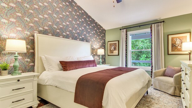 Un dormitorio con cama, dos mesitas de noche, una lámpara de noche, una ventana con cortinas y una silla.