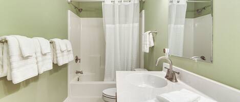 A bathroom with a bathtub, a sink, and a toilet. There are towels hanging on the wall.