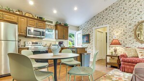 Una cocina moderna con electrodomésticos de acero inoxidable, un comedor con una mesa redonda y sillas, y una sala de estar con un sofá y una alfombra estampada.