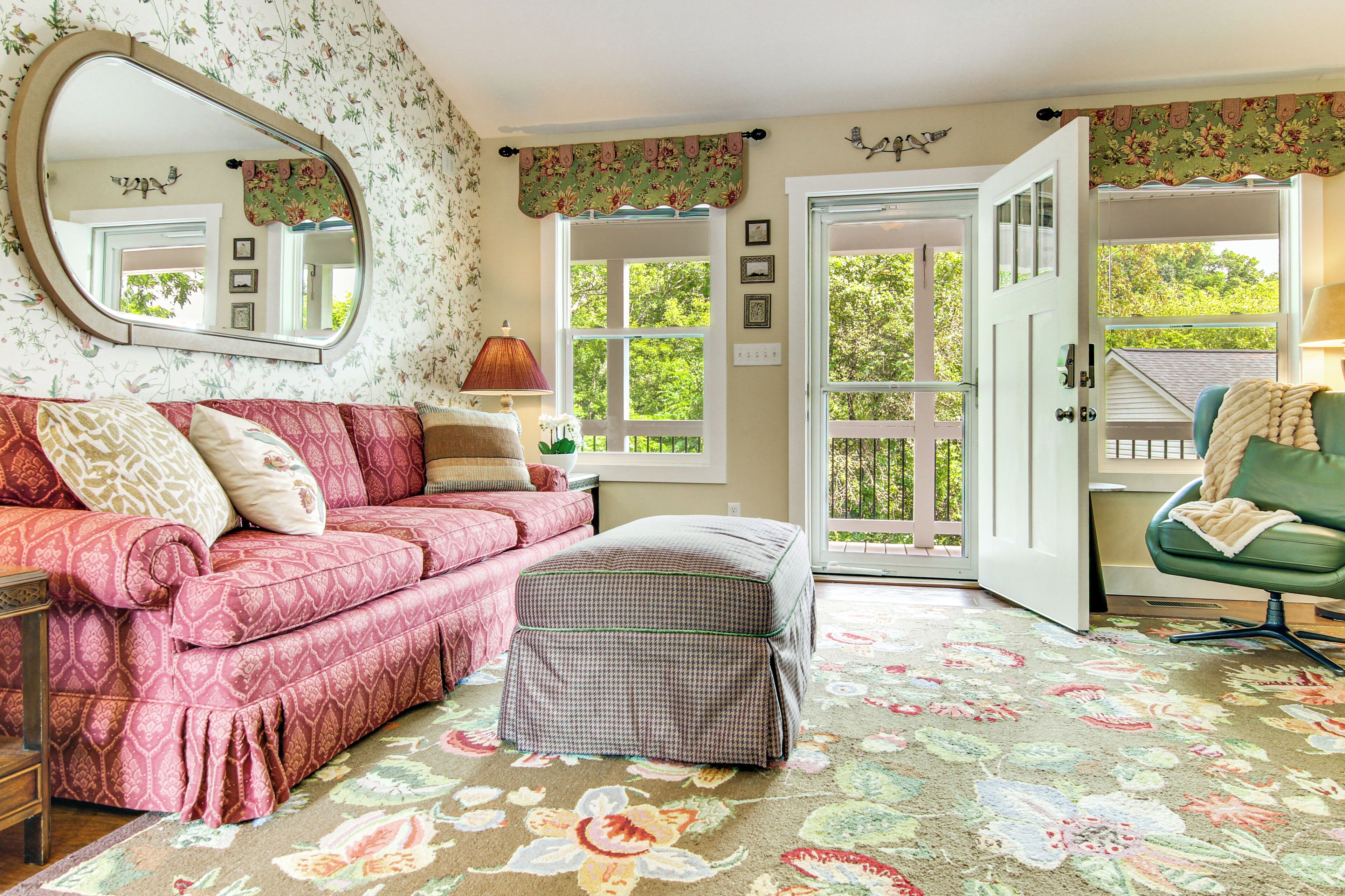 A room with a floral-patterned carpet, a pink sofa, a green armchair, and a round mirror on the wall.