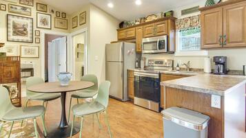 A compact kitchen with a dining area, wooden cabinets, stainless steel appliances, and a wall adorned with framed pictures.