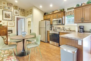 A compact kitchen with a dining area, wooden cabinets, stainless steel appliances, and a wall adorned with framed pictures. - Walk to Waynesville Hot Spots! 'woodland Cottage' (Waynesville)