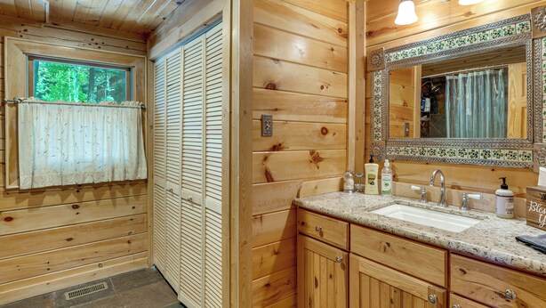 A wooden cabin bathroom with a large mirror, a sink, and a window with a towel.