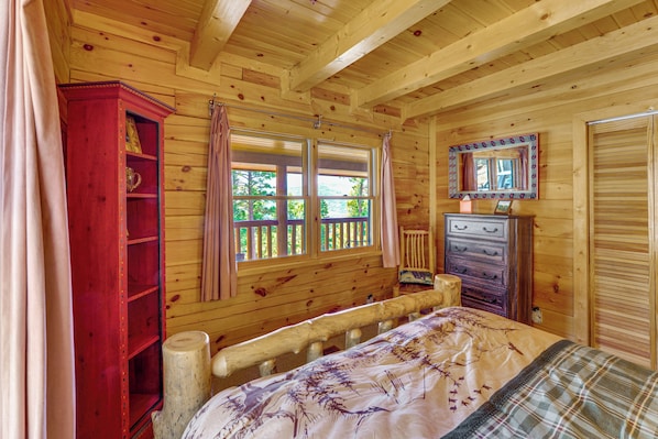 Une chambre dans un chalet en bois, avec un lit, une commode, un miroir et une fenêtre avec des rideaux.