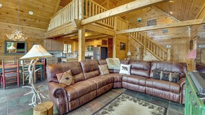 A spacious living area with a leather sectional sofa, a dining table with chairs, a kitchen area, and a staircase leading to an upper level.