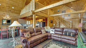 A spacious living area with a leather sectional sofa, a dining table with chairs, a kitchen area, and a staircase leading to an upper level.