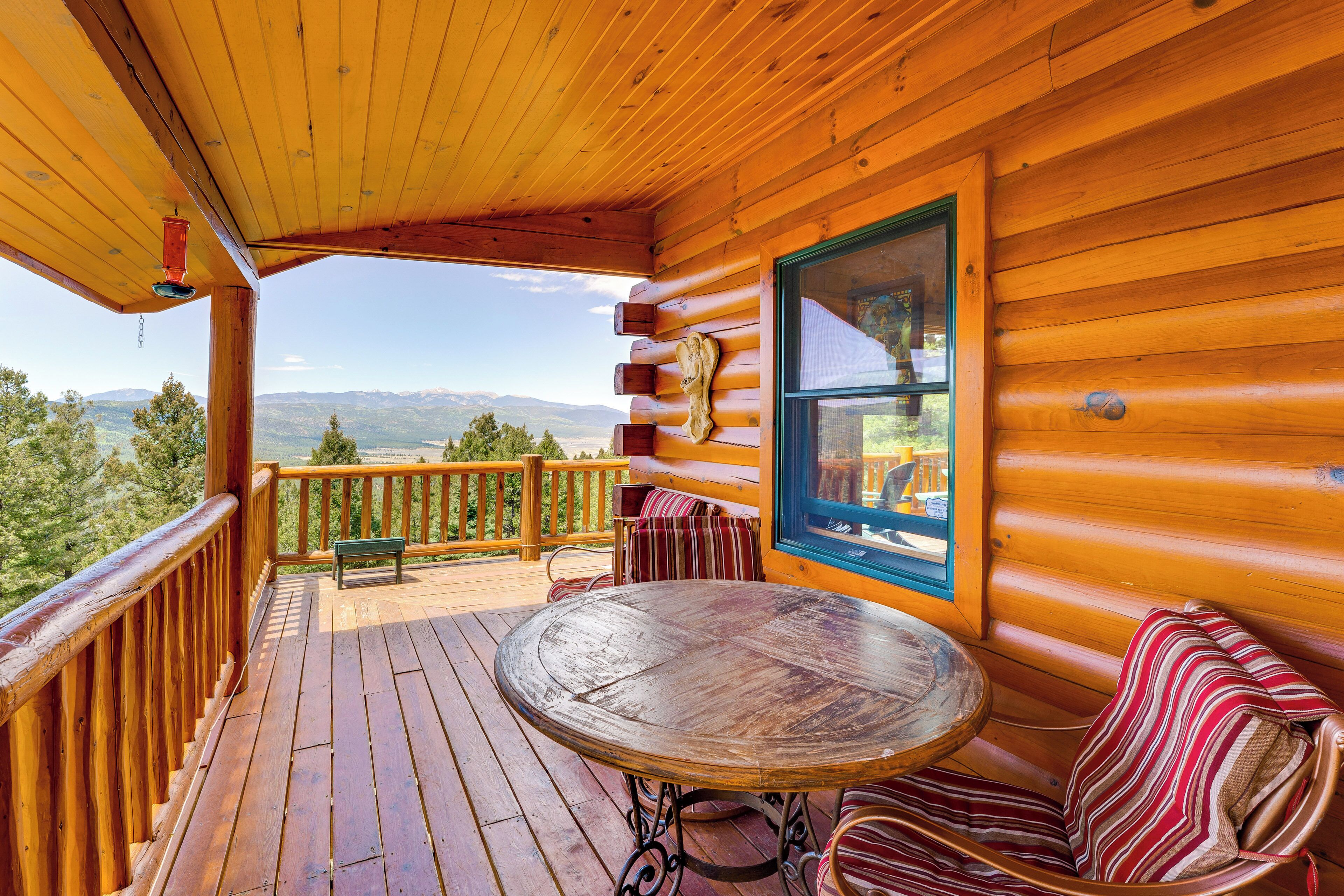 Une terrasse en bois avec une table et des chaises, offrant une vue sur un paysage montagneux.