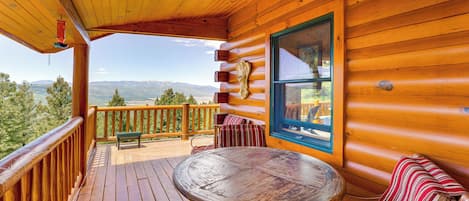 Une terrasse en bois avec une table et des chaises, offrant une vue sur un paysage montagneux.