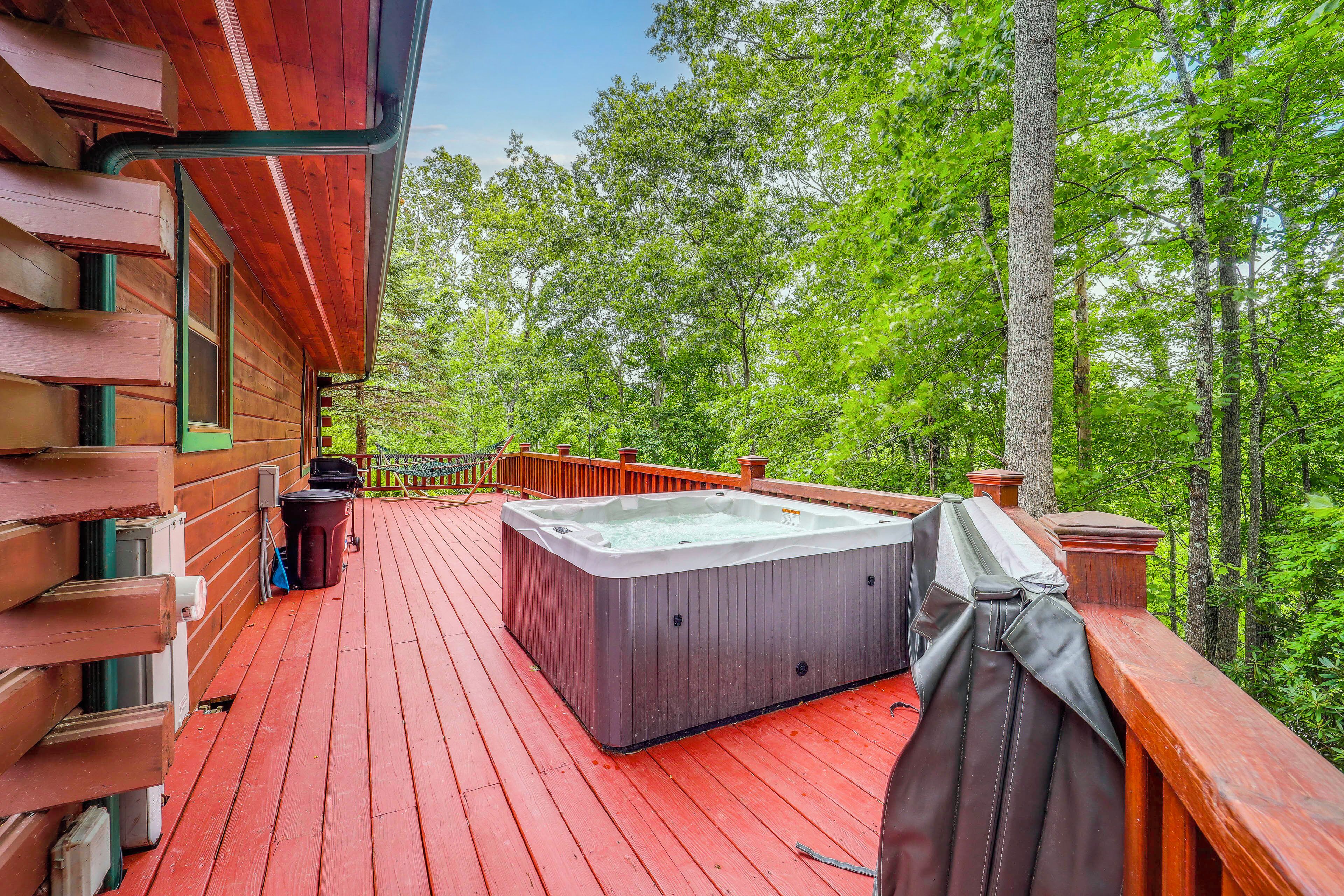 Una terraza de madera con un jacuzzi, rodeada de árboles.
