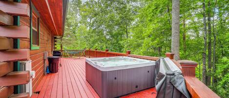 Una terraza de madera con un jacuzzi, rodeada de árboles.