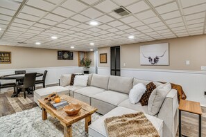 Un salon spacieux avec un canapé d’angle, une table basse en bois et un jeu de fléchettes accroché au mur.