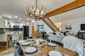 A modern kitchen with white cabinets, a dining area with a wooden table set for four, and a staircase leading to the upper floor. - 'the Blue Goose Chalet': Your Cozy Up North Escape (Gaylord)