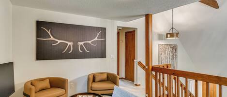 A modern living room with a ceiling fan, a large abstract painting, two leather sofas, a coffee table, and a staircase with wooden railings.