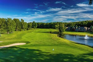 Ein Golfplatz mit Teich, Bäumen und einem Gebäude im Hintergrund.