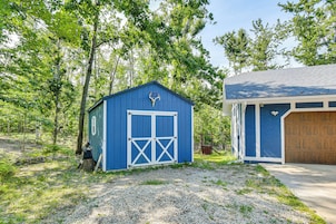 A small blue building with a garage door, surrounded by trees and gravel.