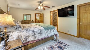 A bedroom with a bed, a ceiling fan, a TV mounted on the wall, and a wooden door. - River Access! Wooded Cabin in Great Cacapon (Great Cacapon)