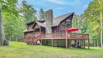 A log cabin with a stone chimney, wooden deck, and a red umbrella.