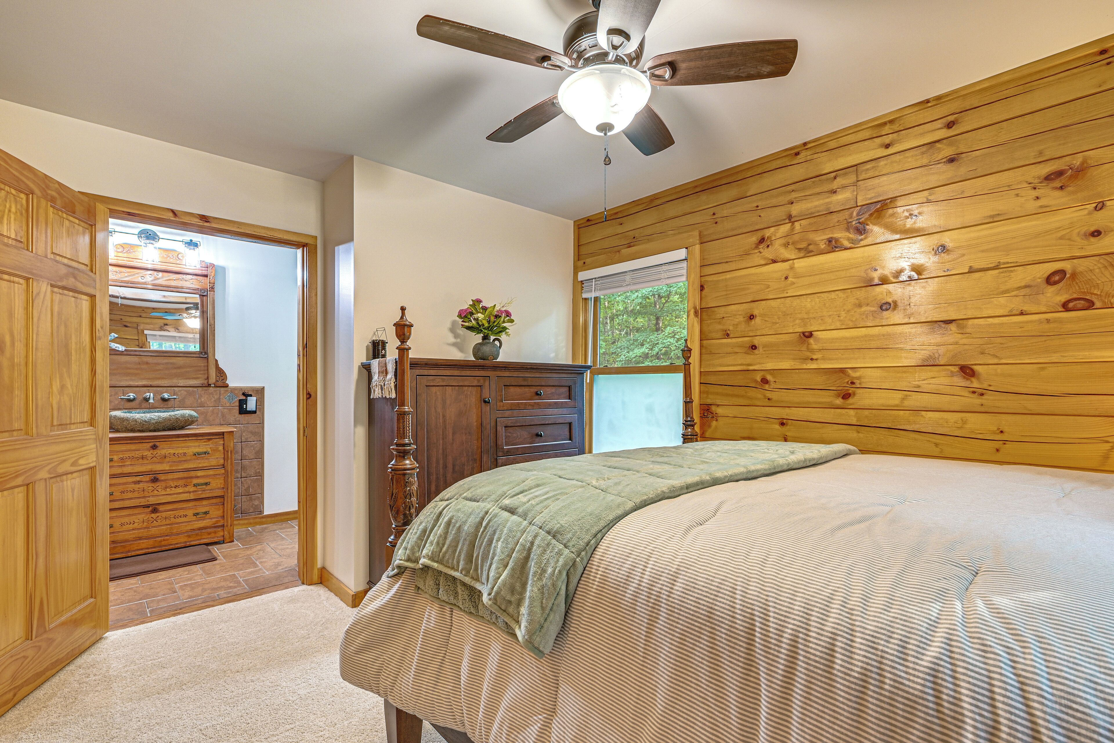 A bedroom with a wooden headboard, a bed with a striped bedspread, a nightstand, a dresser, and a ceiling fan.