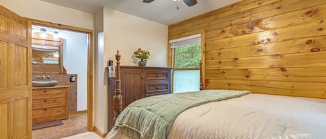 A bedroom with a wooden headboard, a bed with a striped bedspread, a nightstand, a dresser, and a ceiling fan.