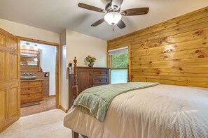 Une chambre à coucher avec une tête de lit en bois, un lit recouvert d’une couvre-lit à rayures, une table de chevet, une commode et un ventilateur de plafond.