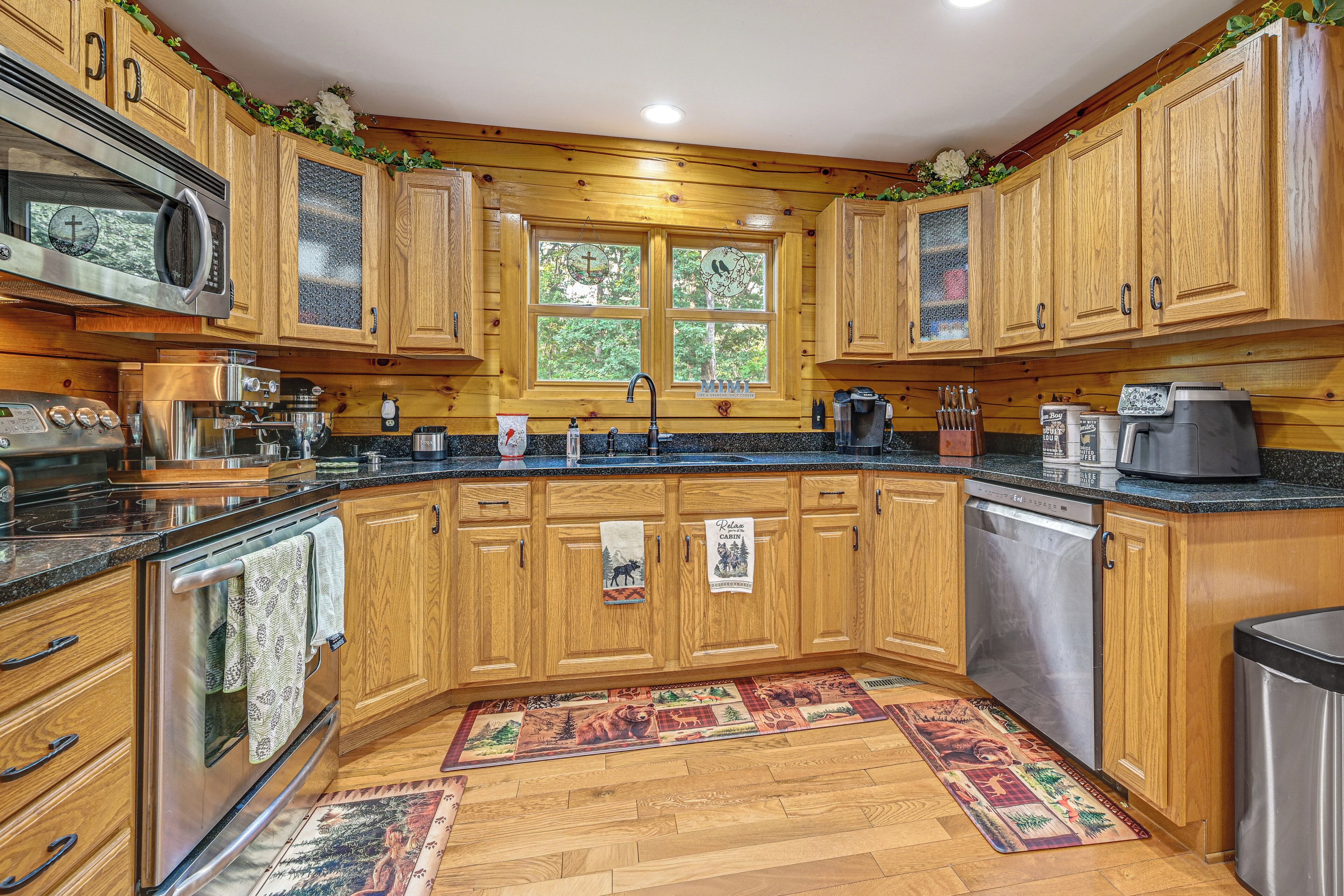 A kitchen with wooden cabinets, a granite countertop, stainless steel appliances, and a window with a view of trees.