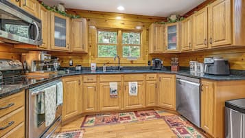 A kitchen with wooden cabinets, a granite countertop, stainless steel appliances, and a window with a view of trees.