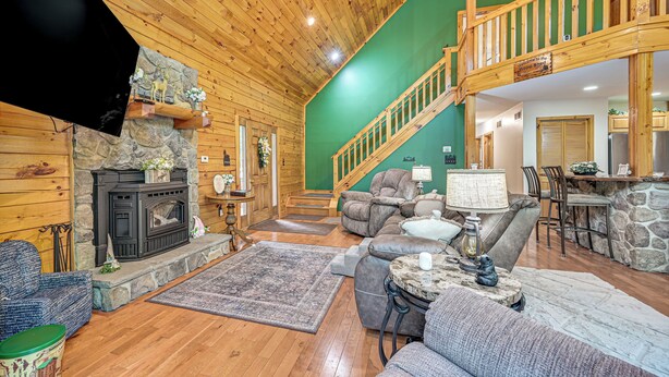 A spacious living area with a fireplace, comfortable seating, a staircase, and a kitchen area. - River Access! Wooded Cabin in Great Cacapon (Great Cacapon)