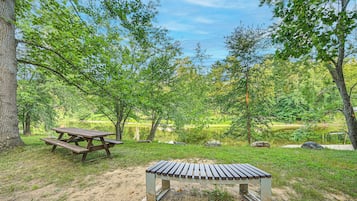 A picnic area with a bench and picnic table surrounded by trees and a lake.
