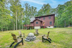 A log cabin with a deck, surrounded by a grassy yard and trees. - River Access! Wooded Cabin in Great Cacapon (Great Cacapon)