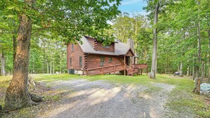 A log cabin with a porch and a gravel driveway. - River Access! Wooded Cabin in Great Cacapon (Great Cacapon)