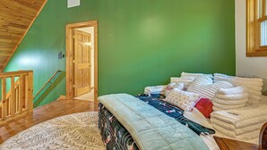 A room with a sloped ceiling, a bed with multiple pillows and blankets, a wooden door, and a window. - River Access! Wooded Cabin in Great Cacapon (Great Cacapon)