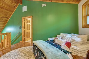 A room with a sloped ceiling, a bed with multiple pillows and blankets, a wooden door, and a window. - River Access! Wooded Cabin in Great Cacapon (Great Cacapon)