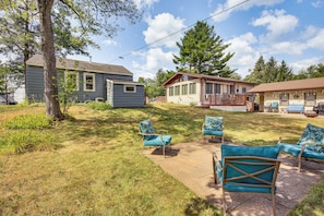 A residential area with a grassy yard, a wooden deck, and a house with a porch. - Shawano Lake Home: Beach Access, Partial Lake View (Shawano)