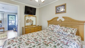 Un dormitorio con cama, televisión, espejo y ventilador de techo.