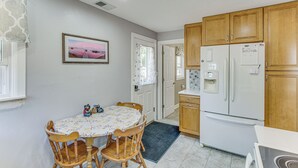 Una cocina con armarios de madera, un refrigerador, una mesa de comedor con sillas y un cuadro en la pared.